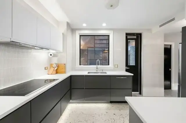 Gold Coast kitchen with gray shaker cabinets, a marble-look quartz island, double wall ovens and glass pendants